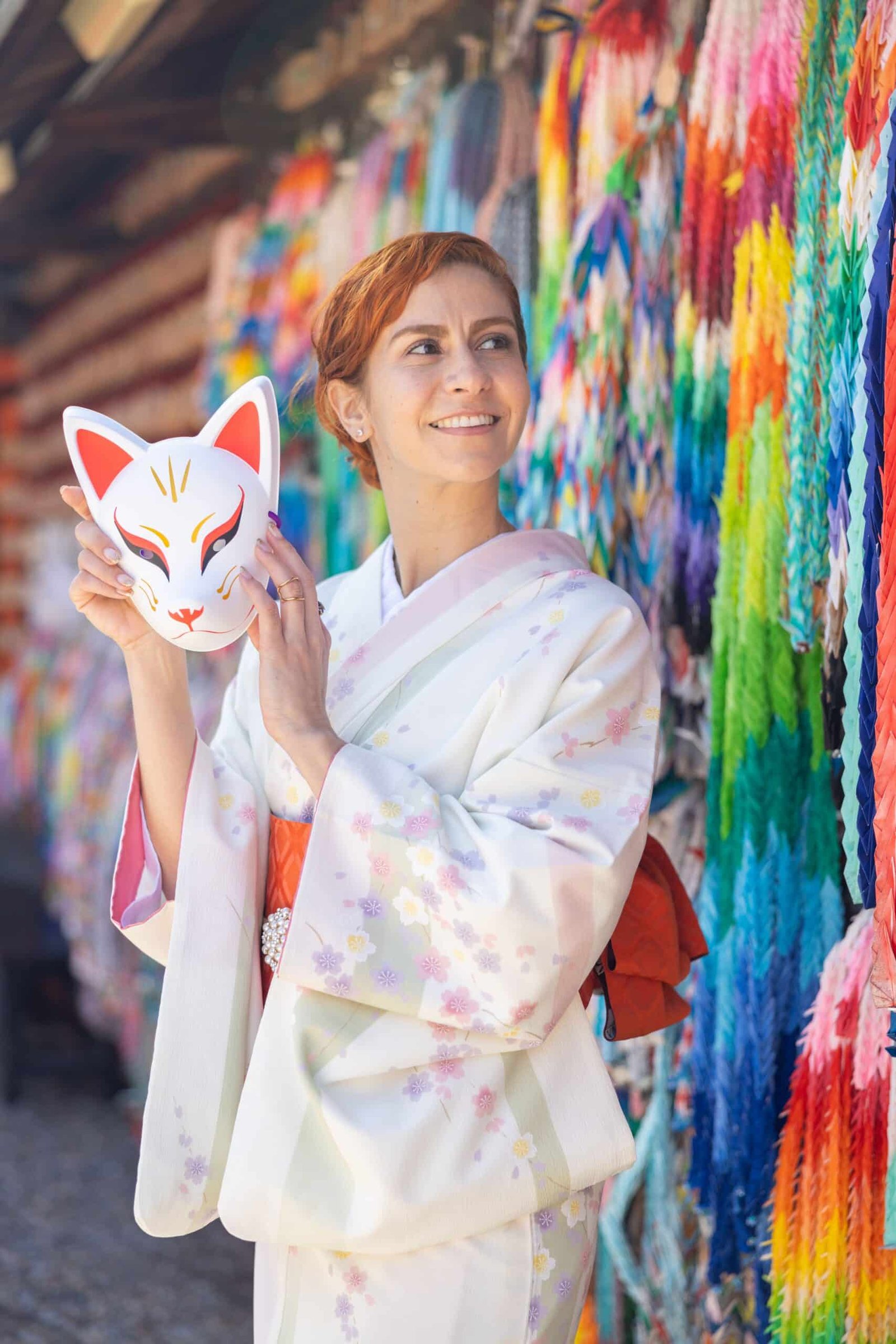 Kalu vestindo um kimono segurando uma máscara de raposa.