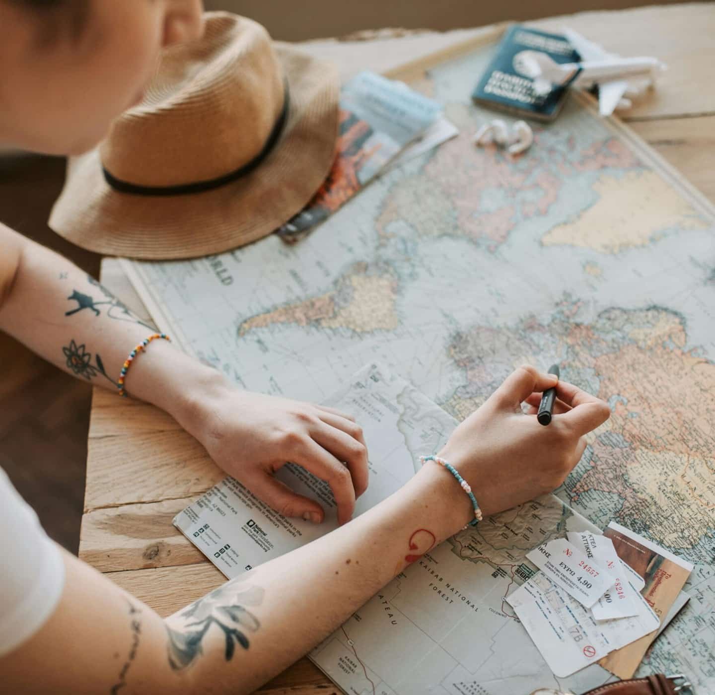Uma mulher com tatuagens no braçõ fazendo anotações de viagem num mapa do mundo.