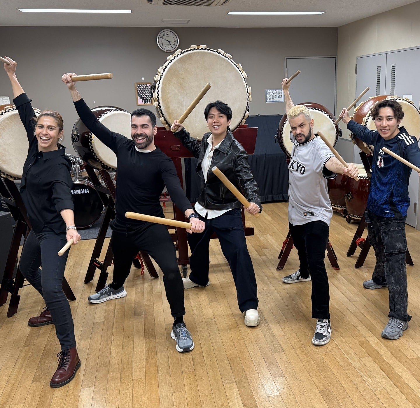 Kalu e um grupo de pessoas posando com bastões em frente a tambores de Taiko.