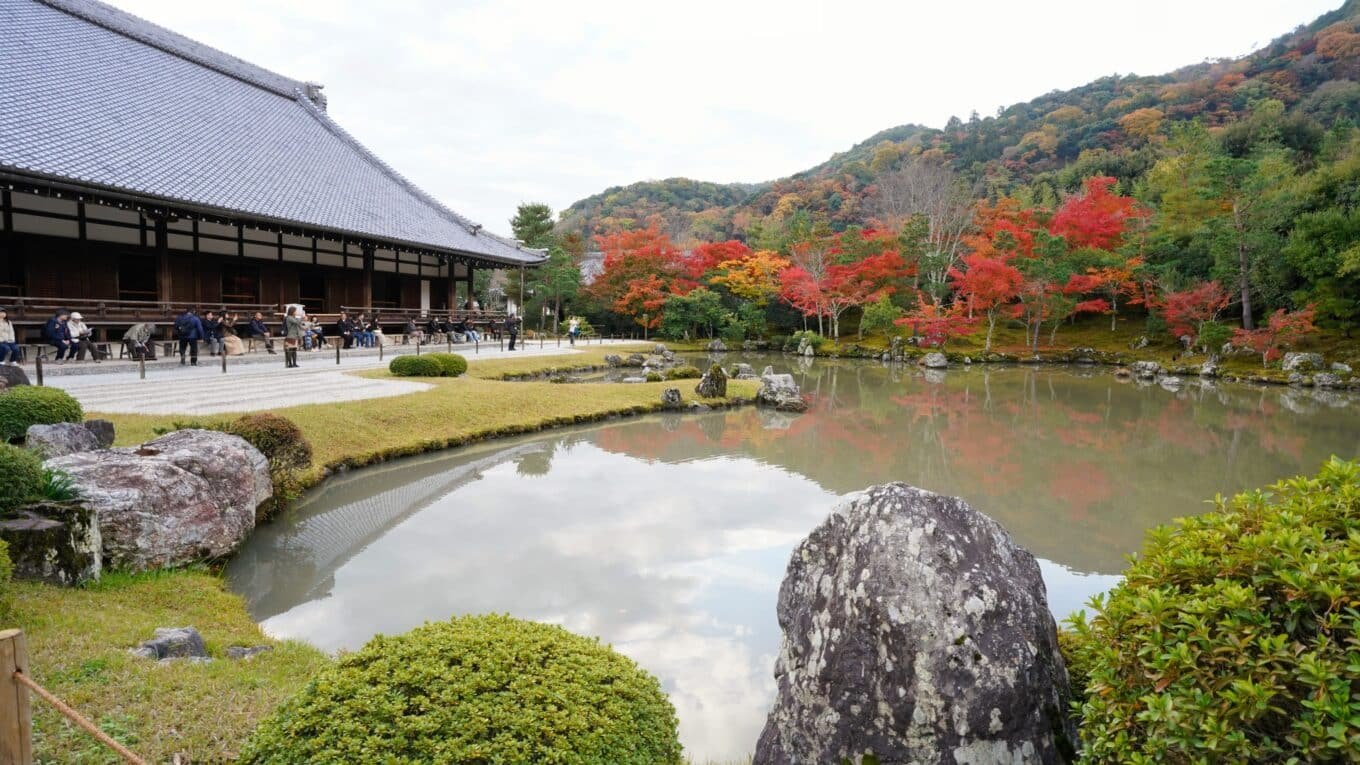 O pavilhão do Tenryu-ji ao lado de seu belo lago, com pessoas tirando foto e cercado de árvores.