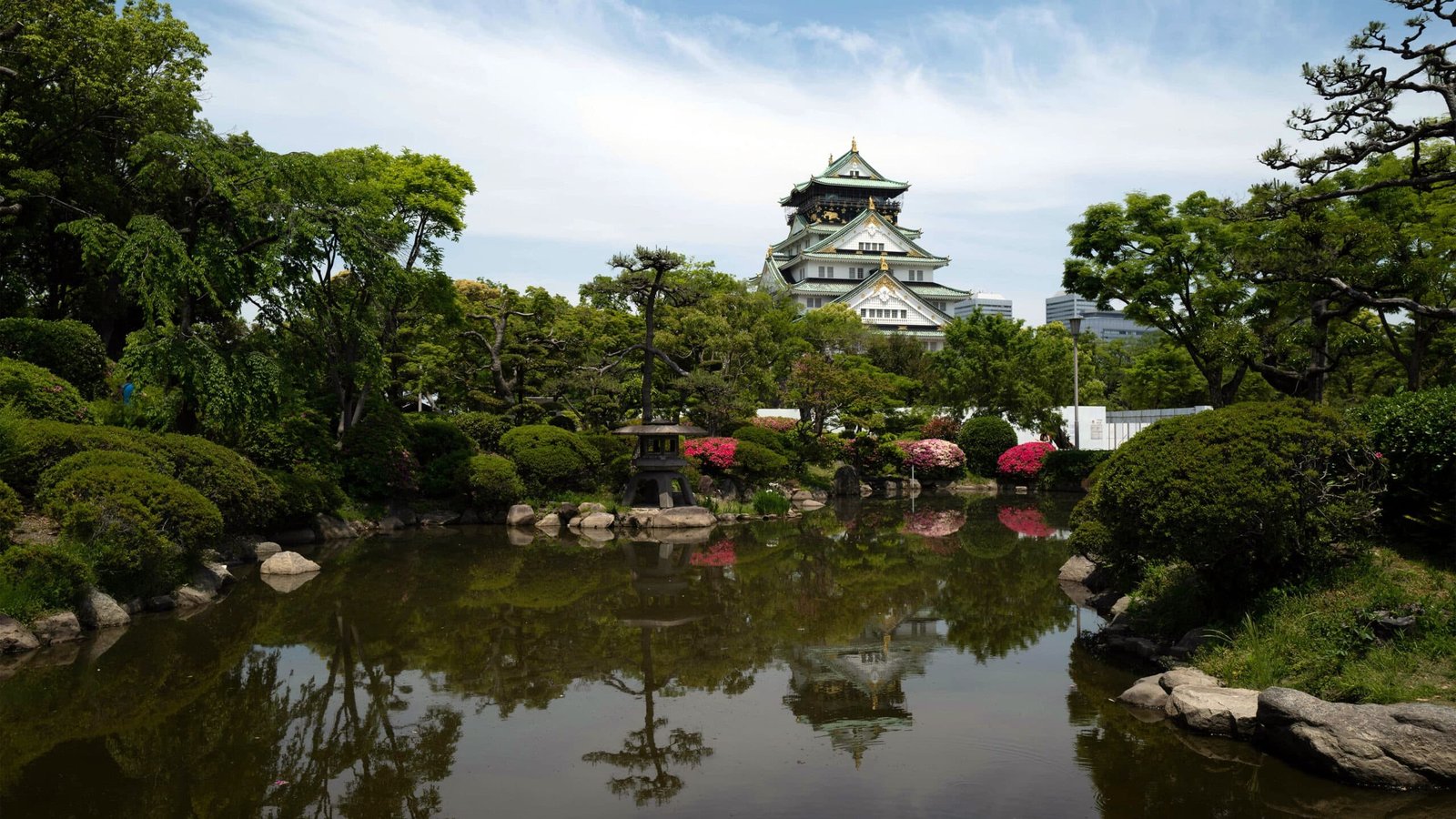 O castelo de Osaka visto do outro lado de um lago cercado de plantas.